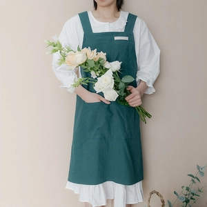Green linen-cotton apron with H-shaped shoulder straps and front pocket for kitchen use