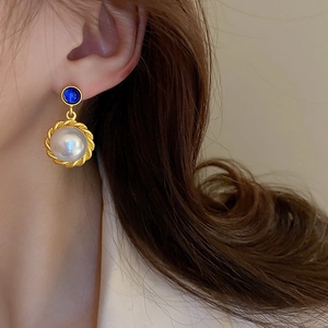 Detail of vintage gold earring with blue gemstone and large pearl on a model's ear