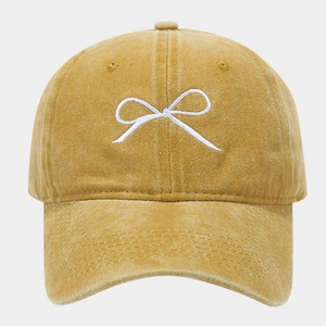 Dettaglio del berretto in cotone lavato giallo con ricamo a fiocco bianco vintage