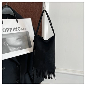Detail view of a black suede tote bag with fringe accents hanging in a stylish setting