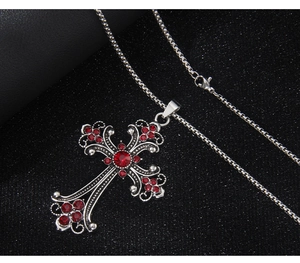 Detail of silver stainless steel cross pendant featuring red gemstones on black background