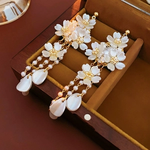 Détail macro de boucles d'oreilles longues à fleurs et perles dans un coffret brun