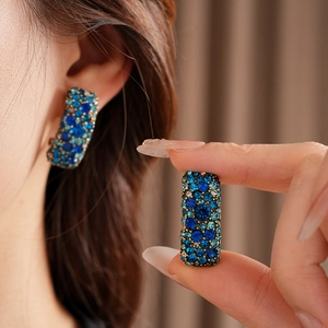 Détail de boucles d'oreilles bohèmes rectangulaires avec strass bleus sur base dorée