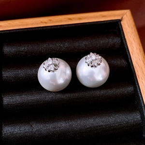 Macro detail of elegant pearl stud earrings with zircon flower set in black velvet box