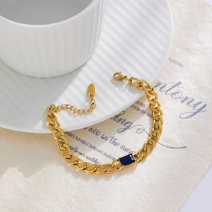 Detail view of gold Cuban chain bracelet with blue rectangular zircon on white dish