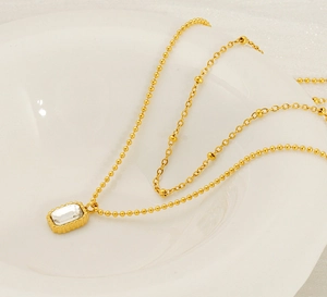 Close-up of golden stainless steel double necklace with emerald-style zircon pendant