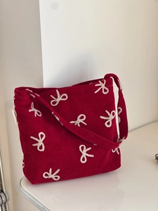 Close-up of red corduroy shoulder bag featuring white embroidered bow patterns