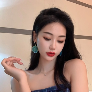 Detailed view of oversized marble textured drop earrings in deep green and blue