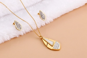 Detail of 18K gold-plated geometric leaf pendant and earrings set on soft background