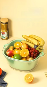 Detail of double-layer kitchen colander set with fresh fruits in green and clear baskets
