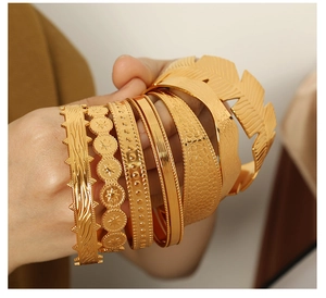 Detail of stacked gold bracelets featuring feather, star, and textured patterns