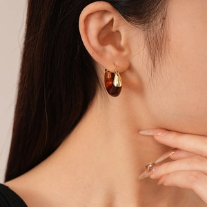 Close-up of Maillard style amber resin and gold metal U-shaped hoop earrings on model