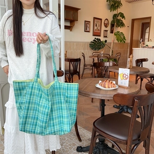 Close-up of a large green plaid canvas tote bag in a cozy cafe setting for women