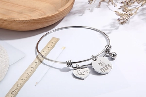 Bracelet cœur argenté avec pendentifs Love mi mama et cloche près d'une règle en bois