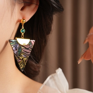 Close-up of vintage golden triangle earrings with green stone on model with soft lighting