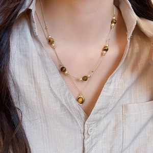 Detail of layered vintage tiger eye necklace featuring gold chains and flower pendant