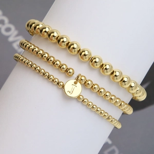 Three-piece gold beaded bracelet set with round initial J charm on white pedestal