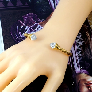 Detail shot of golden twisted cable open bangle featuring rhinestone encrusted cone tips