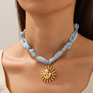 Detail of a gold sun face pendant on a blue patterned fabric chain worn by a model