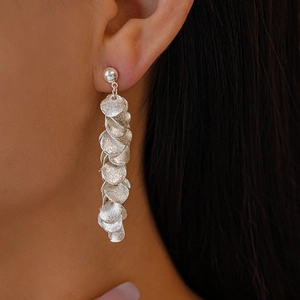 Detail van zilveren kwastjes oorbellen met matte ronde schubben bij een vrouwelijk model