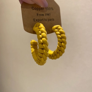Detail of yellow handwoven C-shape copper earrings on kraft card with texture