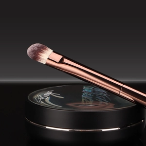 Detail view of premium makeup brush and black cushion foundation on reflective surface