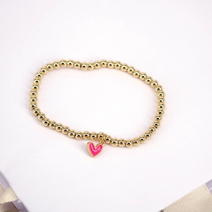 Detail of gold beaded bracelet featuring a pink heart-shaped pendant with gold trim