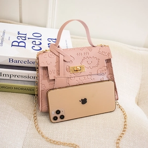 Pink embossed mini chain bag with lock and phone for size reference on white sofa