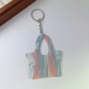 Macro shot of acrylic handbag keychain with pink and teal marble texture on white surface