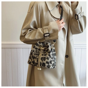 Detail of leopard print plush bucket bag with golden chain and pearl charms on a beige coat