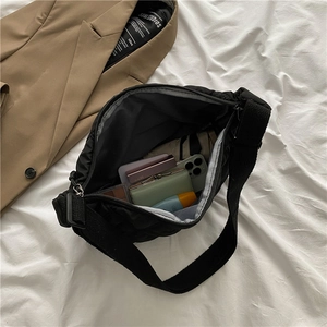 Quilted black nylon crossbody bag with wide strap on white bedding backdrop