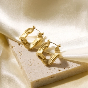 Detail of golden textured geometric earrings on stone with champagne silk background