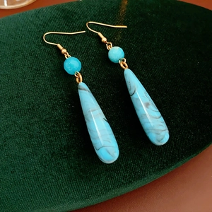 Dettaglio ravvicinato di orecchini bohémien a goccia blu con texture marmorea su velluto