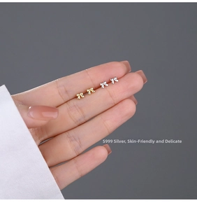 Close-up of mini S999 sterling silver bow stud earrings in silver and gold colors