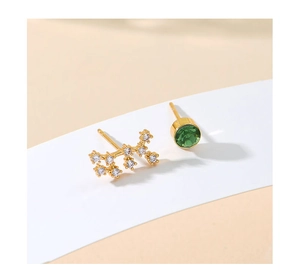 Close-up of asymmetrical gold stud earrings with a green stone and wavy cubic zirconia