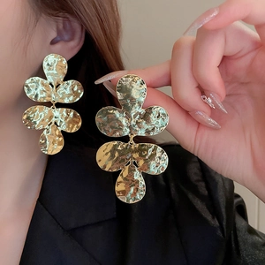 Detail of large gold floral earrings with hammered metal texture on model display