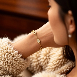 Détail d'un bracelet plaqué or 24 carats avec breloque cœur pavé et pièce au poignet