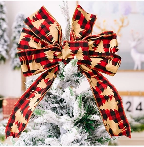 Detail of red black plaid Christmas bow with golden reindeer and tree on snowy pine tree