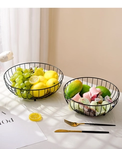 Detail of matte black wire fruit basket with snacks and fresh lemons on white desk