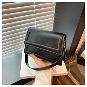 Minimalist black flap handbag on a white book featuring wide strap and square design