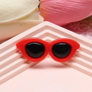 Detail shot of red resin cat eye sunglasses charm on pink steps for DIY crafts