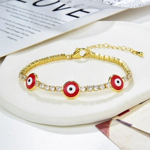 Detail view of a gold lobster clasp bracelet featuring red evil eye charms and cubic zirconia
