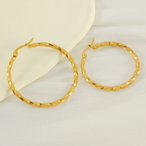 French style gold spiral twisted hoop earrings in titanium steel on white fabric background