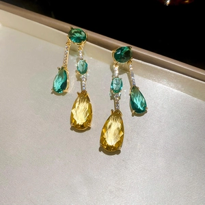 Gros plan de boucles d'oreilles dorées avec zircons verts et jaunes taillés en poire