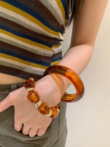 Close-up of amber acrylic geometric bangle and beaded bracelet on a woman wrist