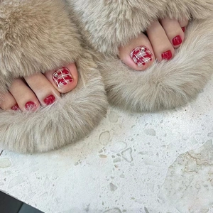 Close-up of red and checkered pattern press-on toenails with rhinestone accents