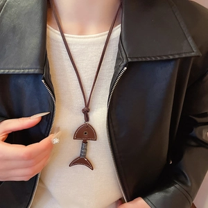 Detailed close-up of dark brown leather and metal fishbone pendant on a model