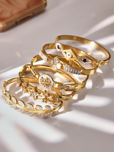 Detail of five gold plated bangles with zircon clover and evil eye in shadow lighting