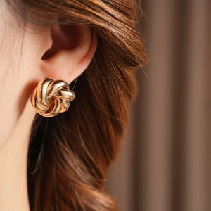 Close-up of a stylish gold knot spiral flower earring worn on a model's ear