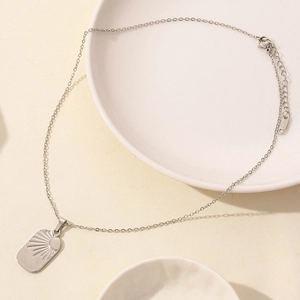 Detail shot of a silver moon and sun star necklace on a white ceramic plate background